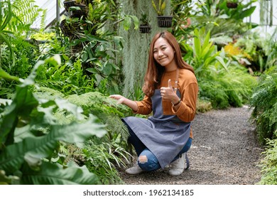 A young asian female gardener making and showing thumbs up hand sign while taking care of plants in the garden - Powered by Shutterstock