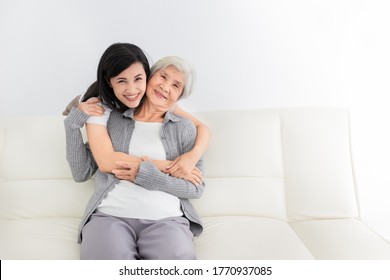 Young Asian Female Hug Old Female In Home, They Feeling Happy And Smile, They Sitting On Sofa, Mother's Day, Happiness Elderly In Family Time