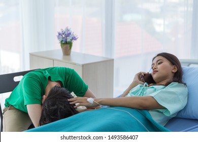 Young Asian female patient is calling to her insurance and business for preparing after dead while her couple sleeping stand by her, on hospital bed in hospital. Wife touches husband's head with love.