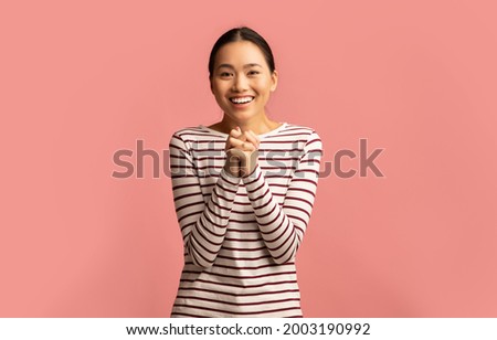 Young asian female pleading and asking for something with clasped hands, excited emotional korean lady looking at camera and saying please while standing isolated over pink background, copy space