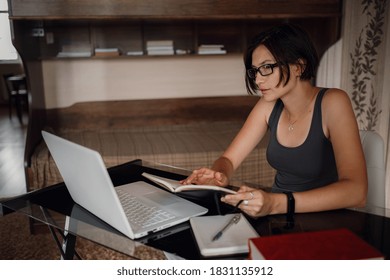 Young asian female student in glasses using laptop, read a book. Cozy office workplace, remote work, E learning concept. - Powered by Shutterstock