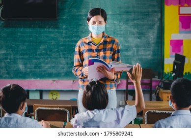 Young Asian Female Teachers Wearing A Medical Face And Students In A Rural Thai Village School Are Learning, Grinding And Raising Their Hands To Answer Teacher Questions.