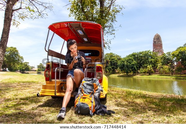 Young asian\
female traveler with backpack traveling sitting on taxi or Tuk Tuk\
and seeing photo on vintage camera with Wat Mahathat background,\
Ayutthaya Province,\
Thailand