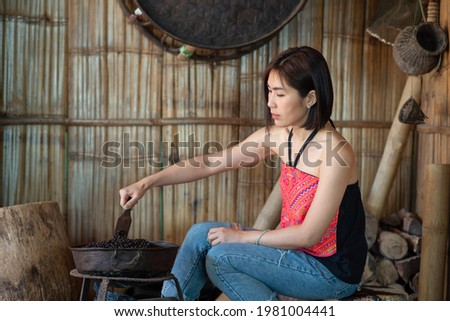 Young Asian female traveler roasting coffee beans using traditional methods at a coffee plantation farm in Ban Phahee, Mae Sai, Chiang Rai Province, Thailand