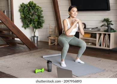 Young Asian Fitness Girl Doing Squats Workout At Home, Follow Online Sport Gym Instructor, Standing On Floor Mat And Smiling, Exercising In Living Room