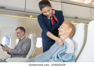 Young Asian Flight attendant woman or air hostess covering a blanket for elderly Caucasian female passengers to sleep well on the plane.