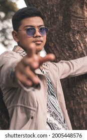 A Young Asian Gangster In Blue Semi Opaque Shades Leaning On A Tree And Pointing At The Camera.