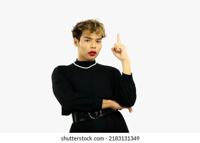 Young Asian Gay Man In Black Dress Wearing Necklace Posing Finger Presenting Pointing On The White Screen Background.