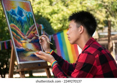 Young asian gay teenager wears rainbow wristband and drawing in the park during his long weekend and his vacation, concept for LGBT people activity and respecting gender diversity around the world.