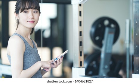 Young Asian Gial Using A Smart Phone In Fitness Gym.