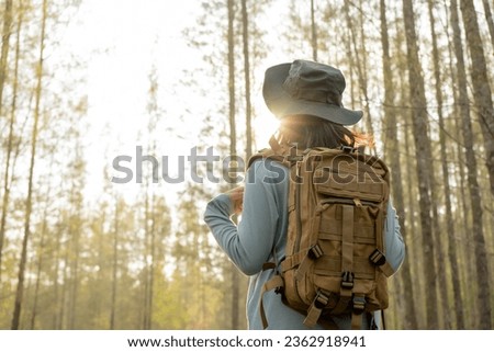Young Asian girl with a backpack and hat hiking in the mountains during the summer season, a traveler walking in the forest. Travel, adventure, and journey concept.