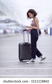 A Young Asian Girl Checking Her Phone While Walking With A Suitcase