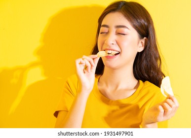 Young Asian girl eating snack on yellow background - Shutterstock ID 1931497901