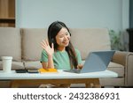young Asian girl engages in online learning, doing homework on her sofa in the living room. video classes, combining comfort and education at home.