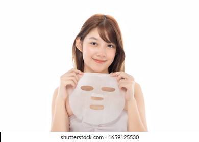 Young Asian Girl With Facial Mask Looking At Camera Over White Background. Cosmetic Procedure. Beauty Spa And Cosmetology.