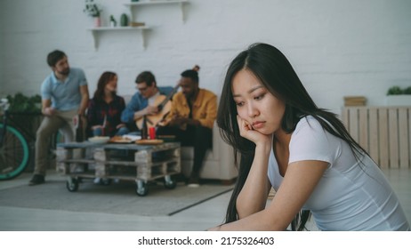 Young Asian Girl Feels Upset And Isolated While Her Flatmates Celebrating Party At Home