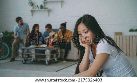 Young asian girl feels upset and isolated while her flatmates celebrating party at home