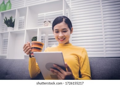 Young Asian Girl Happy Woman Sitting On Sofa Watching Movie With Tablet At Home. After Being Detained At Home Due To The Outbreak Of Coronavirus Covid-19.