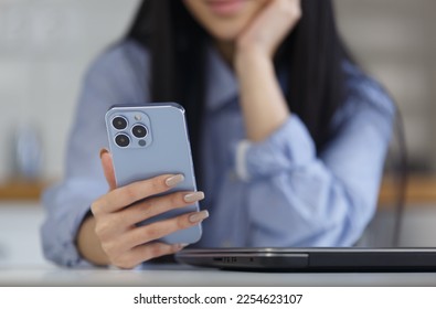 Young asian girl holds blue smartphone with triple camera in hand. BIPOC female from Vietnam using modern mobile phone app