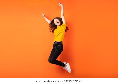 Young asian girl jumping up on orange background