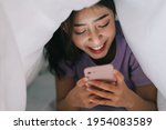 Young Asian girl lying in blanket and using her phone to text with friends on social networks
