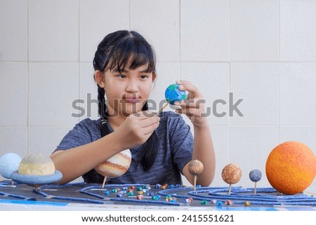 Young Asian girl Making Solar system Model on wooden table at home for her Science Homework project at Elementary school