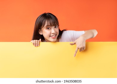Young Asian Girl Pointing Her Finger Down On Yellow And Orange Background