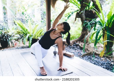 Young asian girl practicing yoga on wooden terrace. Concept of harmony and mental health. Athletic woman with closed eyes wearing sportswear and barefoot on fitness mat. Bali island. Sunny day - Powered by Shutterstock