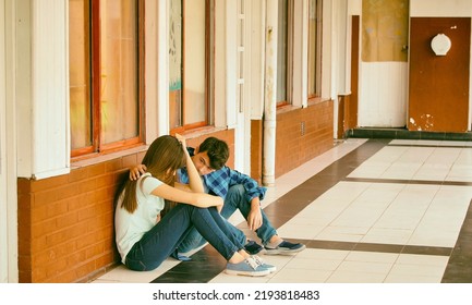 Young Asian Girl Sitting Alone With Sad Feeling At School. Child In Depression Abandoned In A Corridor And Leaning Against Brick Wall. Bullying, Discrimination And Racism Concept.