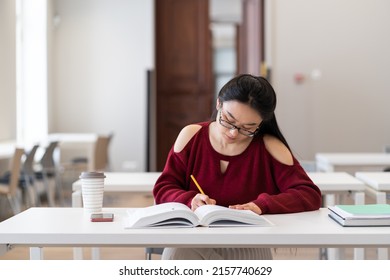 Young Asian Girl Student Making Assessments From Book For Study. Female Preparing For Exam In University, College Or High School, Make Homework Sitting In Empty Classroom Or Library. Education Concept