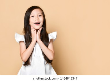 Young Asian Girl Surprised Excited Happy Screaming. Cheerful Kid With Funny Joyful Face Expression On Beige Background