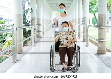 Young Asian Grandchild Taking Care Her Grandmother Sitting On Wheelchair. Grandmother Almost 90 Years Old Was Take Care By Her Granddaughter While Traveling At Park. People Wearing Protective Mask.