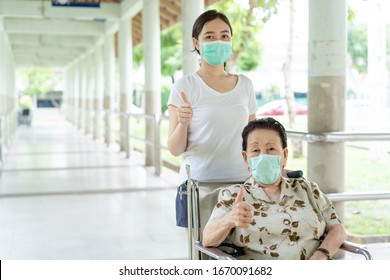 Young Asian Grandchild Taking Care Her Grandmother Sitting On Wheelchair. Grandmother Almost 90 Years Old Was Take Care By Her Granddaughter While Traveling At Park. People Wearing Protective Mask.