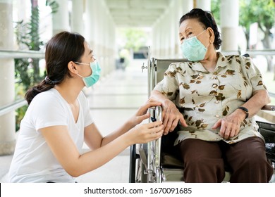 Young Asian grandchild taking care her grandmother sitting on wheelchair. Grandmother almost 90 years old was take care by her granddaughter while traveling at park. People wearing protective mask.