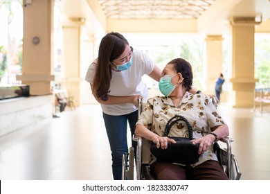 Young Asian Grandchild Taking Care Her Grandmother Sitting On Wheelchair. Grandmother Almost 90 Years Old Was Take Care By Her Granddaughter While Traveling At Park. People Wearing Protective Mask.