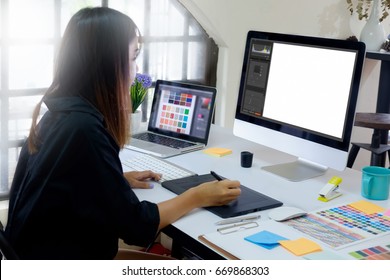 Young asian graphic designer working on computer using digital tablet at office.  Blank screen monitor for graphic display montage.