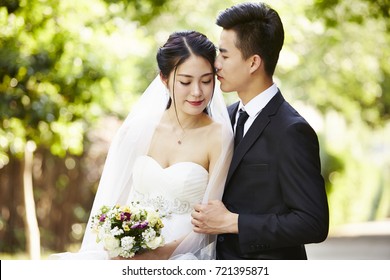 young asian groom kissing bride outdoors during wedding ceremony.