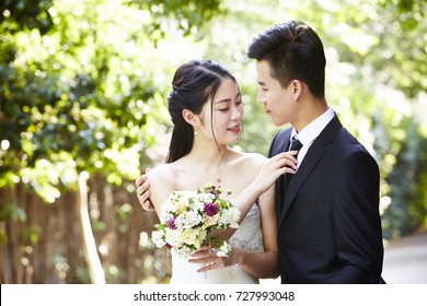 Young Asian Groom Kissing Bride Outdoors During Wedding Ceremony.