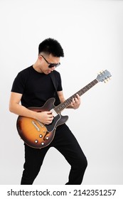 Young asian guy guitarist standing playing solo over isolated white background with a sunburst brown semi hollow body guitar pointing upwards