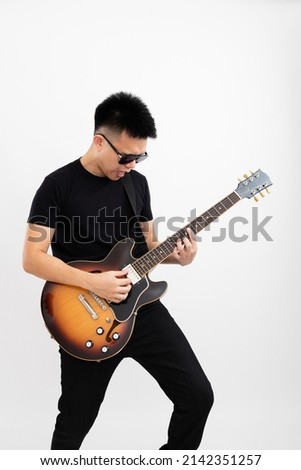 Young asian guy guitarist standing playing solo over isolated white background with a sunburst brown semi hollow body guitar pointing upwards