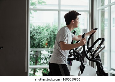 Young Asian Guy On Casual Dress Working In The Gym Using Running Machine. Exercising At Home.