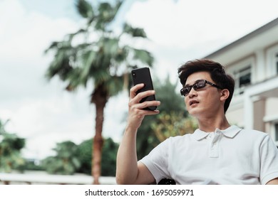 Young Asian Guy On White Shirt Wearing Sunglasses Using Mobile Phone At Resort Villa.