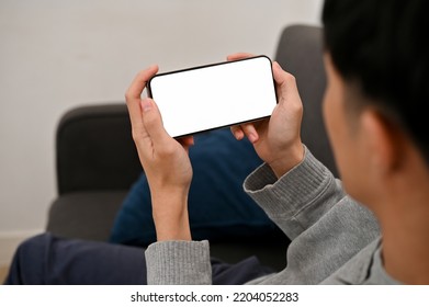 A young asian guy using his smartphone, watching video or playing mobile game. mobile phone white screen mockup. close-up, back view - Shutterstock ID 2204052283