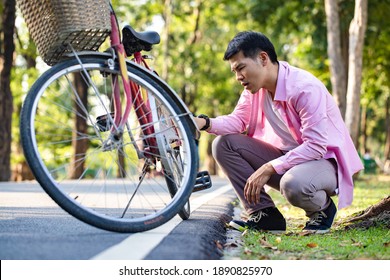 Der junge asiatische Mann checkt und repariert sein Fahrrad im öffentlichen Park. Probleme beim Training auf der Straße. Beheben und Helfen des Konzepts.