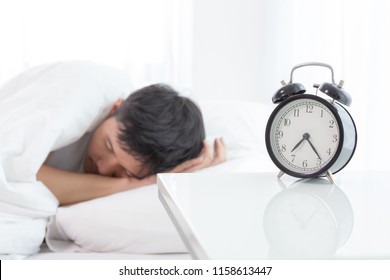 Young asian handsome man sleeping in his bedroom. Boy sleeping with alarm clock in foreground. The time is half pass 7 AM. Wake up in morning of working day concept.
