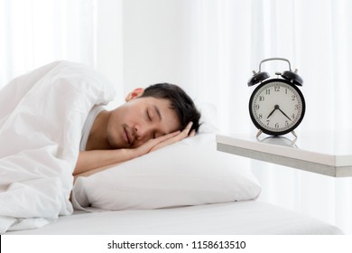 Young asian handsome man sleeping in his bedroom. Boy sleeping with alarm clock in foreground. The time is half pass 7 AM. Wake up in morning of working day. WFH Work From Home concept.