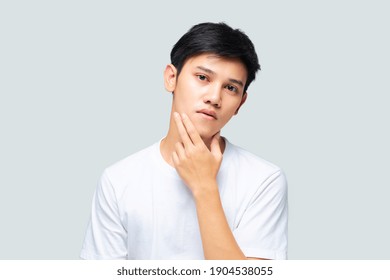 Young Asian Handsome Man Using Hand Touches His Chin To Check His Skin On Isolated Gray Background, Studio Shot. Skincare And Beauty Concept.