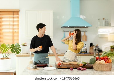 Young Asian Happy Active Family Couple Dancing Laughing Together Preparing Food At Home, Carefree Joyful Husband And Wife Having Fun Cooking Healthy Romantic Dinner Meal Listen To Music In Kitchen.