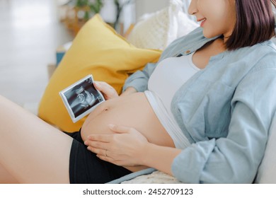 Young Asian happy pregnant woman is and holding ultrasound 4d scan image touching her belly. Family plan, pregnancy, motherhood, people and expectation, child and Maternity prenatal care concept - Powered by Shutterstock