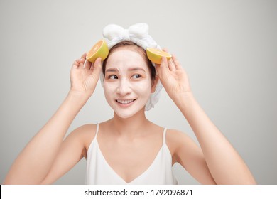 Young Asian having white facial clay mask and holding orange piece.